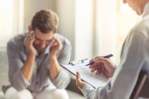 Stressed man with head in hands talks with a therapist about his anxiety. Anxiety therapy in Savannah, GA can help you cope with stress and overwhelm and other anxiety symptoms.