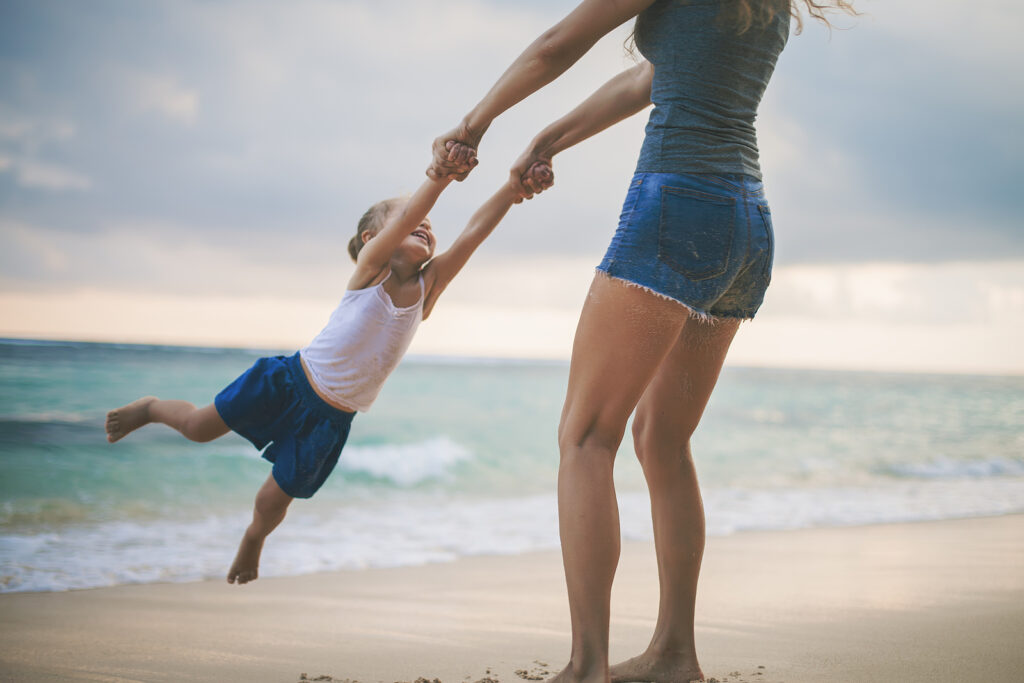 A mother swings her smiling child around by the arms on the shore. This could represent the benefits that therapists in Savannah, GA can offer for parents. Learn more about counseling for teenagers and Savannah counseling by searching “therapy for teens savannah, ga” today.
