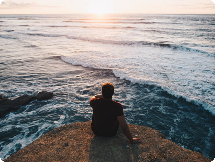 Man sitting on a cliff watching the ocean waves and sunset